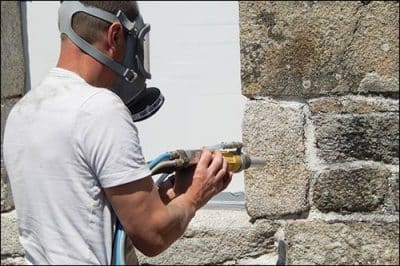 Une personne doté d'équipement nettoyant une façade en pierre